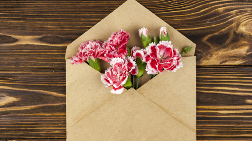 brown-envelope-with-red-carnation-flowers-over-wooden-desk_23-2148058567