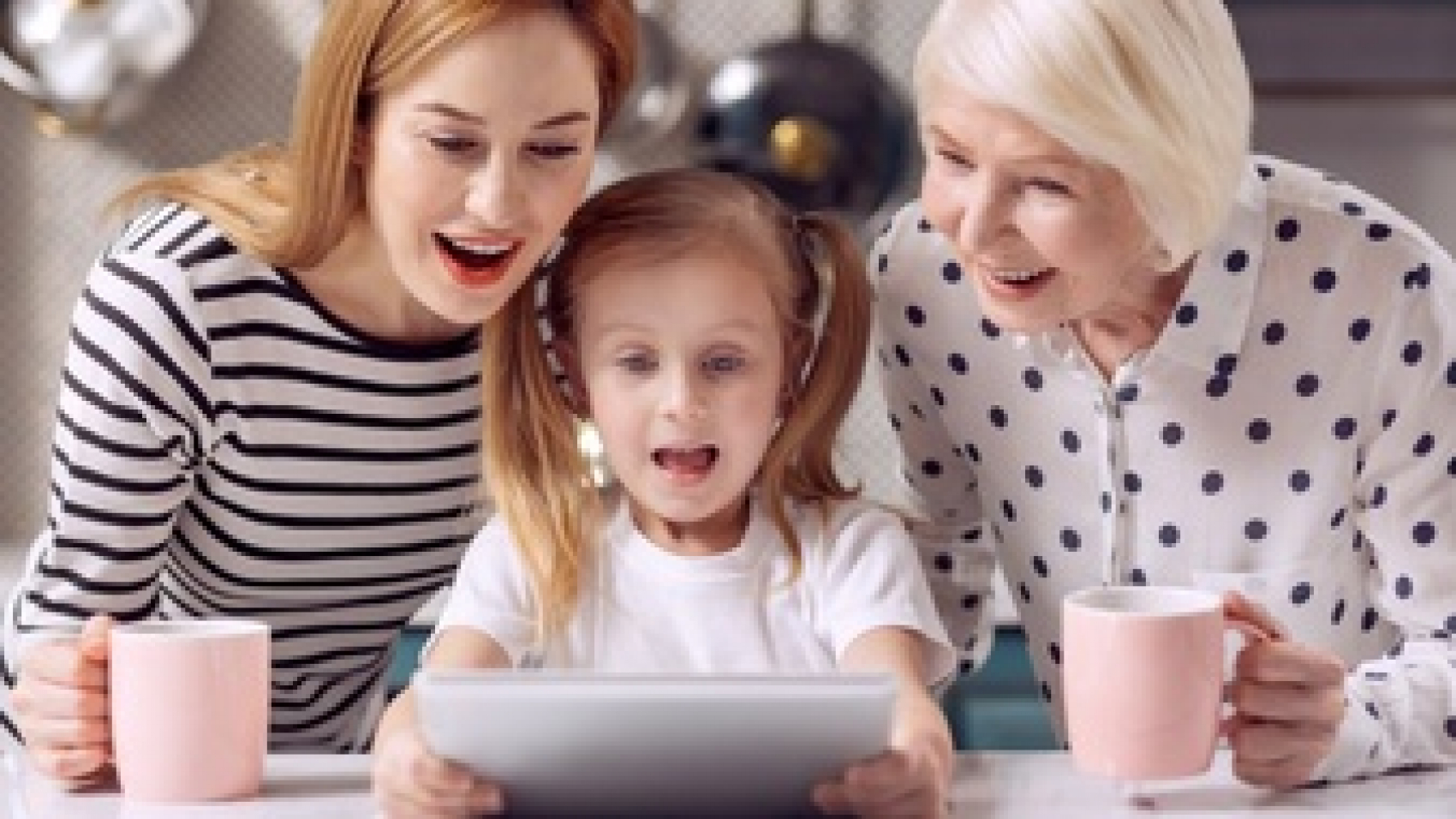 exciting-cartoon-pleasant-little-girl-watching-a-cartoon-on-tablet-together-with-her-grandmother-and-mother-drinking-coffee-from-pink-mugs-while-looking-amused-by-plot-twists_259150-25392